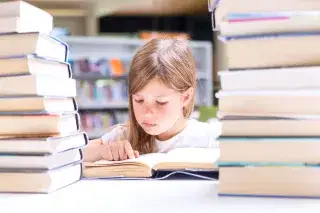 210107_kind-lesen-buch_shutterstock_468809222 Kind zwischen Bücherstapeln liest ein Buch